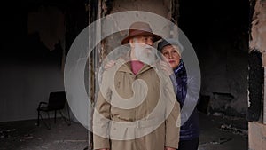 Sad senior woman walking to devastated man standing in ruined bombed house thinking. Old hopeless couple talking hugging