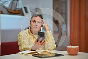 Sad senior woman in yellow sweater with smartphone and mask