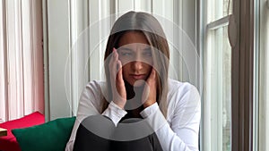 Sad sepressed young woman crying sitting on a window at home