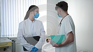 Sad serious Caucasian man and woman in medical uniform discussing ill patient sleeping in ward walking away leaving