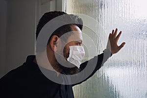 Sad serious man loo at window during quarantine because of world epidemia, virus, coronavirus