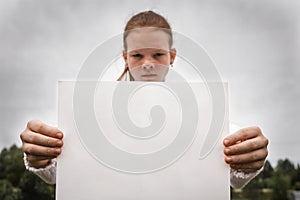 Sad serious teenager girl holding white poster with free copy space for text. Poster or paper blank, placard in person hands