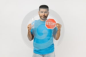 Sad serious unshaven man holding red stop symbol and empty plastic bottle, Earth protection.