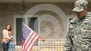 Sad serviceman leaving house looking wife and daughter hugging background, duty