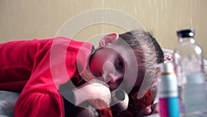 A sad sick boy is lying on the bed with a toy bear, in front of him are medicines that he does not want to take.