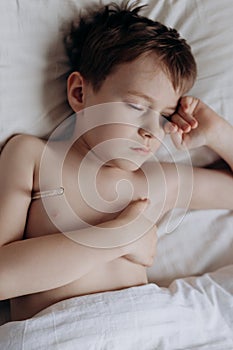 sad sick boy with thermometer lying in bed