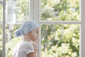 Sad sick child with cancer wearing blue headscarf during treatment