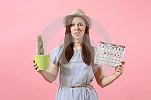 Sad sickness woman in blue dress holding green cactus, periods calendar for checking menstruation days isolated on pink