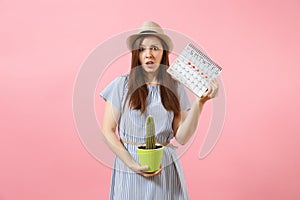 Sad sickness woman in blue dress holding green cactus, periods calendar for checking menstruation days isolated on pink