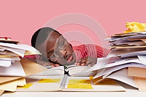 Sad sleepy overworked male scientist leans head on table, being tired of doing scientific work, studies papers, writes