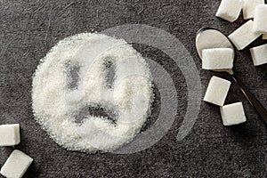 A sad smiley drawn on a pile of sugar. Sugar harm concept