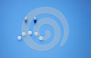 Sad smiley face made of blue and white tablets and pills on blue background top view with copy space for text.