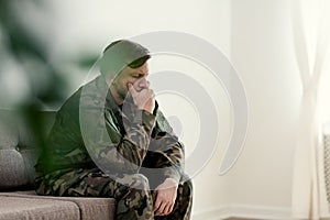 Sad soldier in uniform covering his mouth while sitting on a sofa