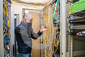 A sad specialist took up his head at the sight of problems with wiring in the server room. Facepalm technician. Incorrect