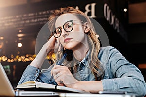 Sad student girl sitting in cafe in front of laptop preparing for exams. Woman takes boring online training course.