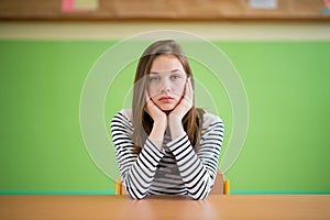 Sad student sitting in classroom with her head in hands. Education, high school, bullying, pressure, depression.