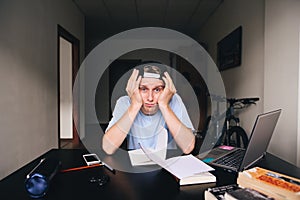 A sad student sitting at a work desk at a house near a laptop and books. Teaching at home. Homework.