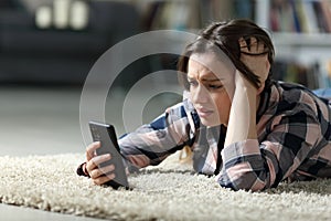 Sad teen checking phone on the floor at home