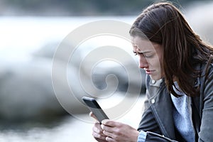 Sad teen complaining checking smart phone on the beach