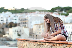 Sad teen complaining sitting on a ledge on vacation