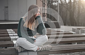 Sad teen girl on a bench in the park. Single girl outdoor. Lonely sad girl