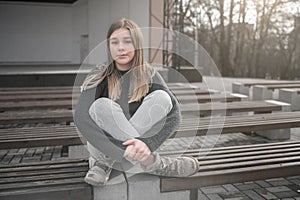 Sad teen girl on a bench in the park. Single girl outdoor. Lonely sad girl