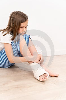 Sad teen girl with orthopedic plaster on her foot sitting on the floor.