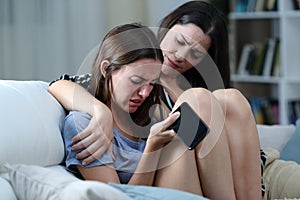 Sad teen with phone being comforted by her sister photo