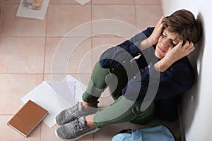 Sad teenage boy sitting on floor indoors. Bullying at school