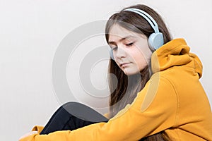 A sad teenage girl, 12-13 years old, sits in headphones sweatshirt on a white background copy space for text. Adolescent problems