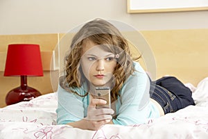 Sad Teenage Girl In Bedroom With Mobile Phone