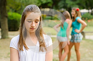 Sad teenage girl rejected by other teenage girls in park