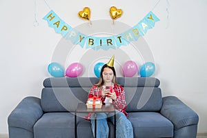 A sad teenage girl sits alone at home with a cake in a room decorated in honor of her birthday, looking at the phone and waiting