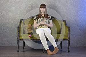 Sad teenage girl sits on green sofa. On gray background. Studio.