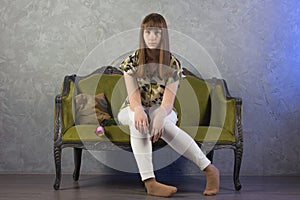 Sad teenage girl sits on green sofa. On gray background. Studio.