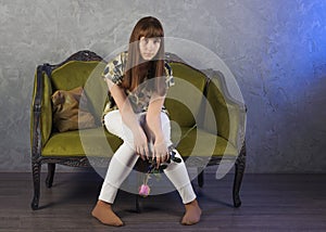 Sad teenage girl sits on green sofa. On gray background. Studio.