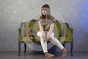 Sad teenage girl sits on green sofa. On gray background. Studio.