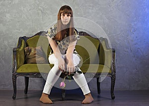 Sad teenage girl sits on green sofa. On gray background. Studio.