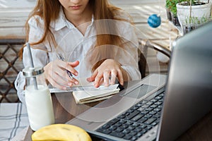 A sad teenage girl sits in her pajamas and learns remotely via the Internet during quarantine. On the table are