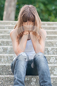 Sad teenage girl sitting alone on the stairs in summer