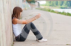 Sad teenage girl sitting alone in urban environmen