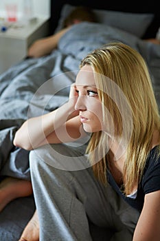 Sad Teenage Girl Sitting In Bedroom Whilst Boyfriend Sleeps