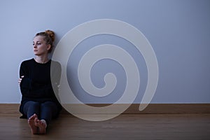 Sad teenage girl suffering from loneliness, sitting alone on the floor, copy space on empty wall