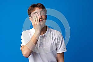 Sad teenager boy failed, touching face against blue background