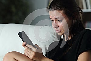 Sad teenager checking phone cyber bullying messages