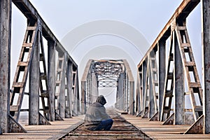 Sad teenager in depression sitting on a bridge at the sunset.