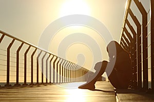 Sad teenager girl depressed sitting in a bridge at sunset photo