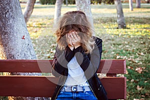 Sad teenager girl sitting on the bench in autumn park. Crying young girl in depression