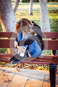 Sad teenager girl sitting on the bench in autumn park. Crying young girl in depression