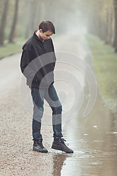 Sad teenager putting foot in puddle